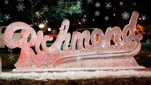 An illuminated ice sculpture of the word "Richmond" with snowflakes in the background, set at night.