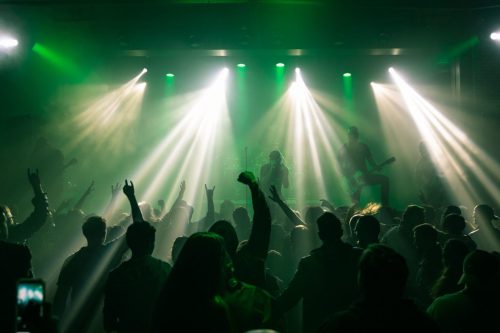 A lively concert scene with a crowd enjoying the performance, illuminated by green lights and beams.