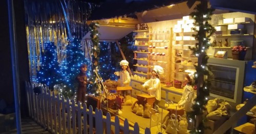 A festive display featuring decorated trees, lights, and figures of chefs in a cozy shop setting.