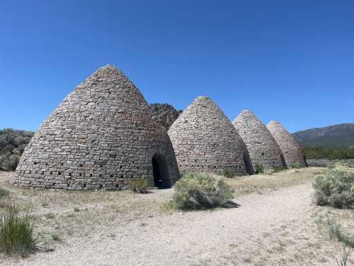 Four stone beehive-shaped kilns stand in a desert landscape under a clear blue sky.