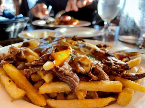 A plate of loaded fries topped with shredded beef, cheese, and sauce, with a blurred background of diners.