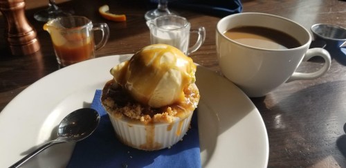 A dessert with ice cream and caramel sauce on a crumbly base, served with coffee and cream on the side.