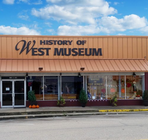 Exterior of the History of West Museum, featuring a sign and decorative pumpkins in front, under a blue sky.