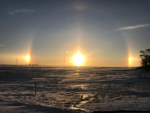 A stunning winter landscape featuring three sun halos in a clear sky over a snowy field.