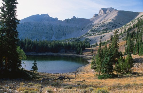 A serene mountain landscape featuring a calm lake surrounded by trees and rugged peaks under a clear sky.