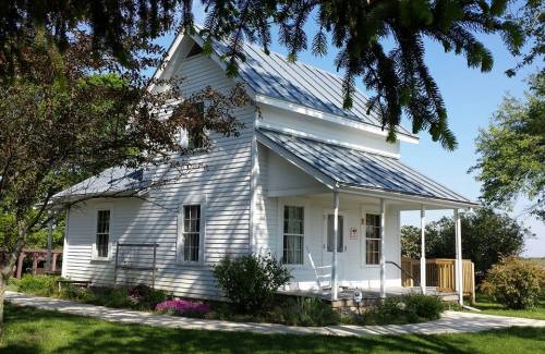A charming white house with a metal roof, surrounded by greenery and flowers, under a clear blue sky.