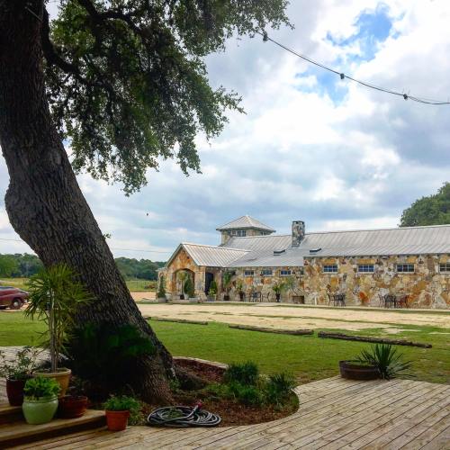 A rustic stone building with a metal roof, surrounded by greenery and a wooden deck under a cloudy sky.