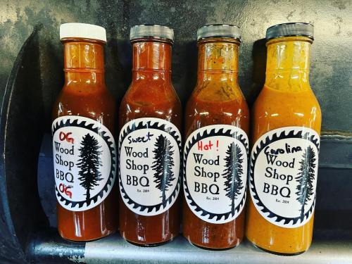 Four bottles of BBQ sauce labeled OG, Sweet, Hot, and Carolina, each with a woodshop-themed design.