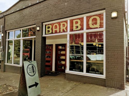 Exterior of a barbecue restaurant with large "BAR B Q" sign, featuring a menu display and a directional sign outside.