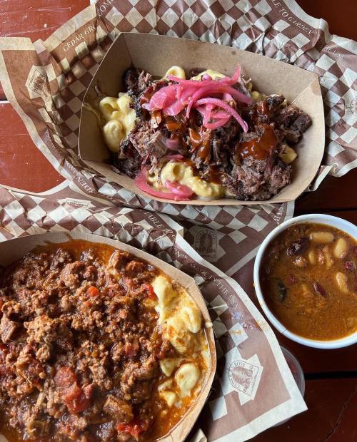 Two trays of food: one with smoked meat and mac and cheese topped with pickled onions, and another with chili and beans.