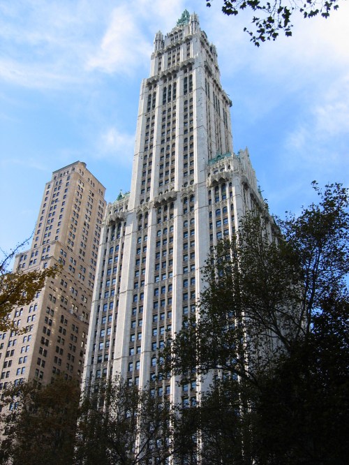A tall, historic skyscraper with ornate details, surrounded by trees and a blue sky.