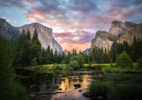 A serene river flows through a lush valley, framed by towering cliffs and a colorful sunset sky.