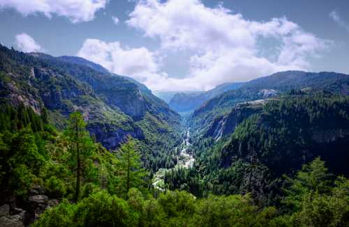 A panoramic view of a lush green valley surrounded by mountains under a partly cloudy sky.