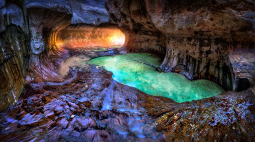 A stunning cave interior with vibrant colors, featuring a glowing pool of turquoise water and textured rock formations.
