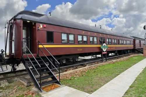 A vintage red train car with "Pennsylvania" lettering, parked on tracks under a cloudy sky.