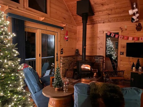 Cozy cabin interior with a Christmas tree, wood stove, and festive decorations, creating a warm, inviting atmosphere.