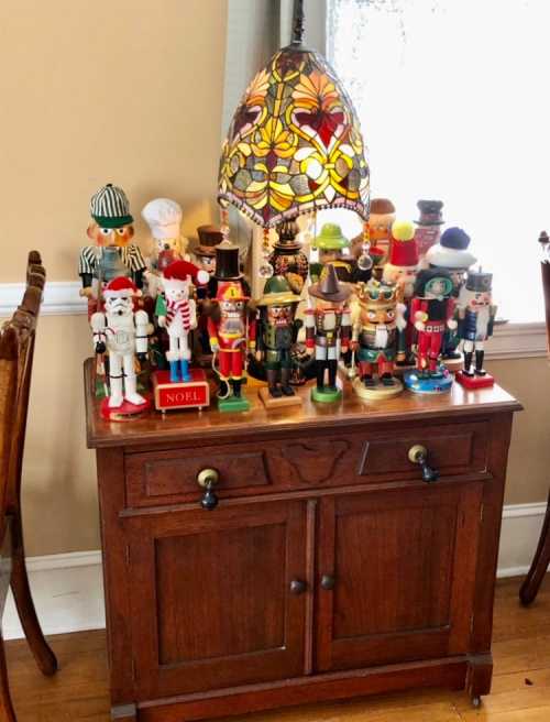 A wooden cabinet displays a collection of colorful nutcracker figurines and a stained glass lamp.