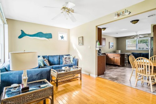Bright living room with blue couch, whale decor, and wooden dining area visible in the background. Sunlight streams in.