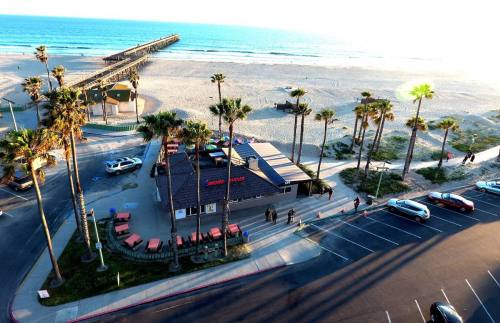 Aerial view of a beachside restaurant with palm trees, a pier, and the ocean in the background.