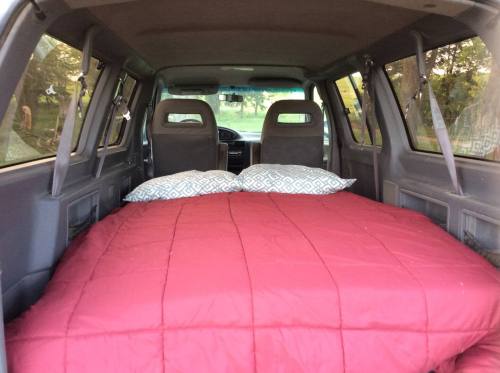 A cozy sleeping area with a red quilt and pillows set up in the back of a vehicle.