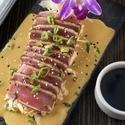 Sliced seared tuna on a bed of cabbage, drizzled with sauce, garnished with green onions and an orchid.