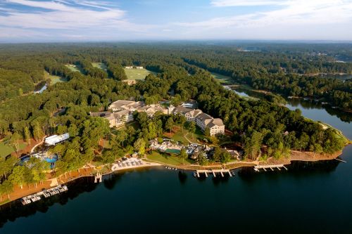 Aerial view of a lakeside resort surrounded by lush greenery and calm waters, with docks and recreational areas visible.