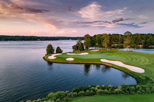 A scenic view of a golf course by a lake, featuring sand traps and lush greenery under a colorful sky.
