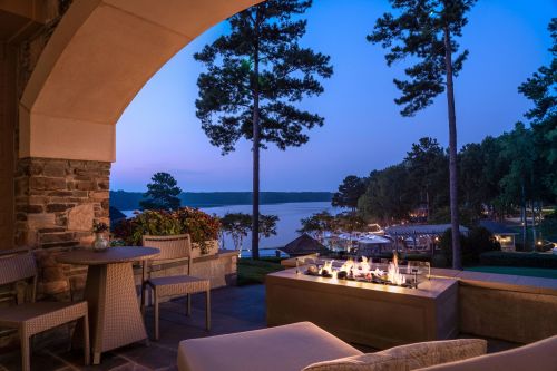 A serene lakeside view at dusk, featuring a cozy seating area and a fire pit surrounded by trees.