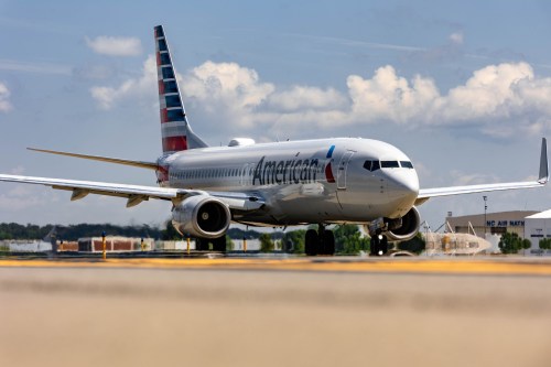 An American Airlines Boeing 737 taxiing on an airport runway under a partly cloudy sky.