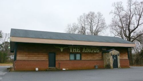 Exterior of a building labeled "The Angus," featuring a wooden facade and a stone entrance.