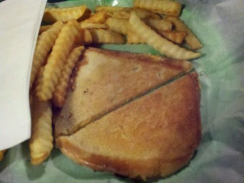 A plate with a grilled cheese sandwich cut in half, accompanied by crinkle-cut fries on a green paper liner.