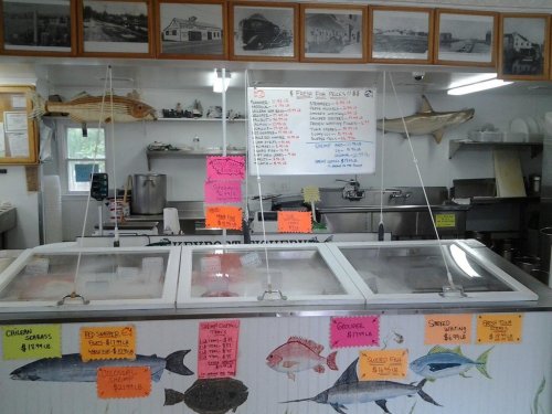 A seafood market display with glass cases, colorful price signs, and black-and-white photos on the wall.