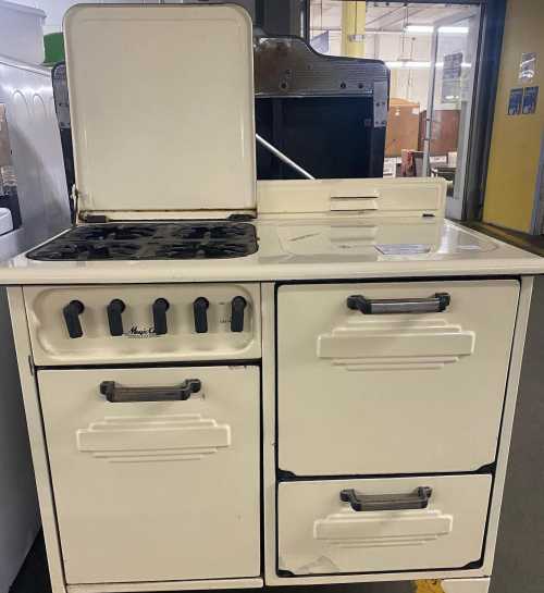 A vintage white kitchen stove with a raised lid, four burners, and two drawers on the side.