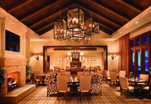 Elegant restaurant interior with high ceilings, a fireplace, and stylish seating under decorative chandeliers.