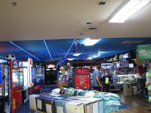 A colorful arcade with game machines, a token dispenser, and a family browsing items in a vibrant, well-lit space.