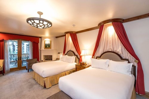 A cozy hotel room featuring two queen beds, elegant curtains, a fireplace, and a balcony with outdoor views.