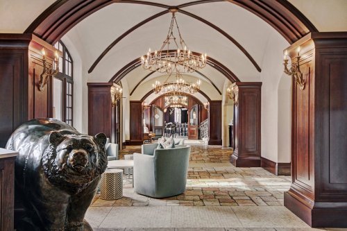 Elegant hallway with arched ceilings, chandeliers, and a bear sculpture, featuring cozy seating areas.