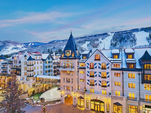 A picturesque winter scene of a charming hotel with snow-covered mountains and ski slopes in the background.