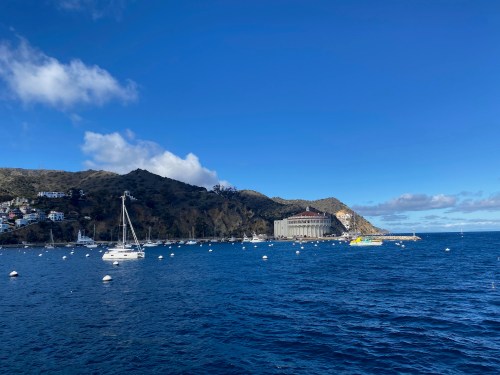 A scenic view of a harbor with sailboats, mountains, and a clear blue sky.