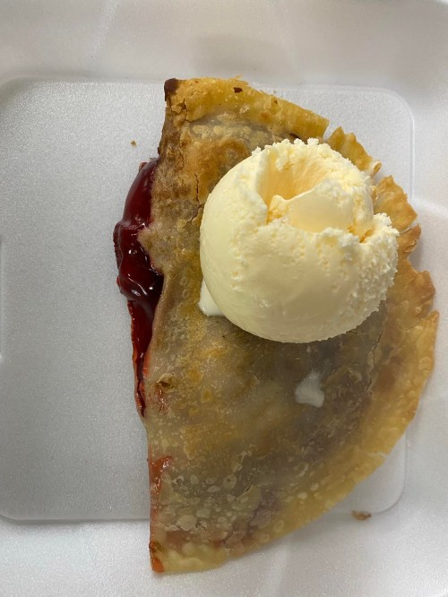 A crispy fried pastry filled with red fruit filling, topped with a scoop of vanilla ice cream on a white plate.