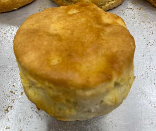 A freshly baked biscuit with a golden-brown top, resting on a silver baking sheet.