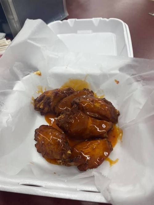 A takeout container with several saucy chicken wings on a bed of white paper.