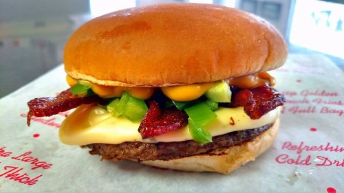 A juicy burger with a beef patty, melted cheese, bacon, green peppers, and creamy sauce on a soft bun.