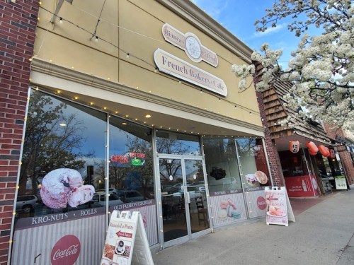 Exterior of a French bakery café with a sign, large windows, and decorative lights, showcasing pastries and an "Open" sign.