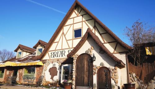 A charming, fairy-tale style building with a thatched roof, stone accents, and a sunny blue sky.