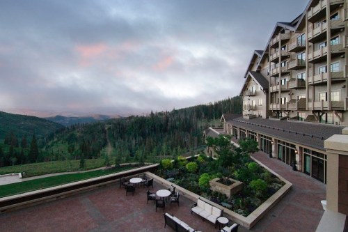 A scenic view of a mountain resort with a patio, surrounded by lush greenery and cloudy skies.