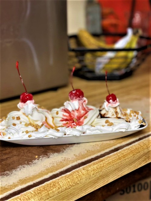 A dessert plate with three ice cream sundaes topped with whipped cream, cherries, and caramel drizzle.