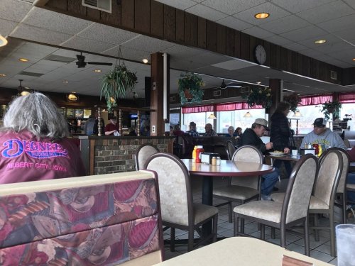 A cozy diner interior with patrons seated at tables, enjoying meals amidst wooden decor and plants.