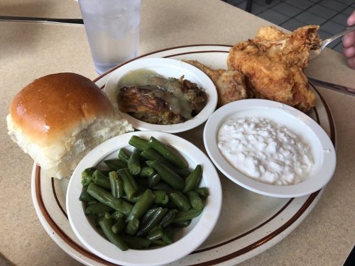 A plate of fried chicken, green beans, coleslaw, stuffing with gravy, and a roll, served with a glass of water.