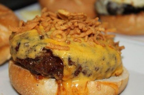 Close-up of a cheeseburger topped with melted cheese and crispy onion strings on a toasted bun.